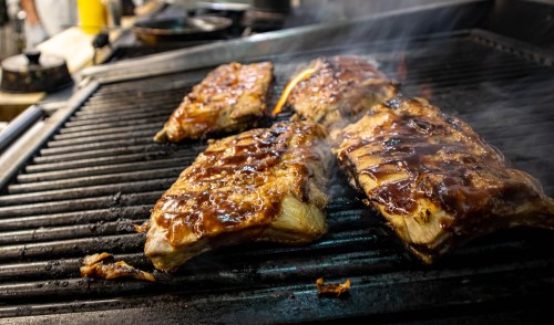 Grilled meat sizzling on a barbecue grill, coated in a glossy sauce with smoke rising around it.