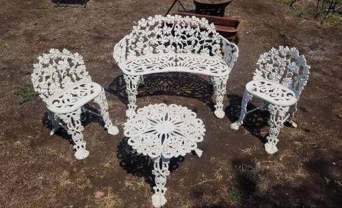 A vintage white metal patio set featuring a floral design, including a bench, two chairs, and a round table.