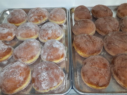 Two trays of freshly baked doughnuts, one with powdered sugar and the other with a cinnamon sugar coating.