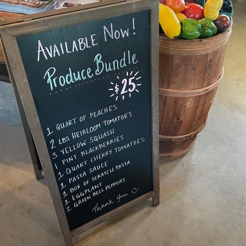 Chalkboard listing a $25 produce bundle with items like peaches, tomatoes, squash, and more, alongside colorful vegetables.