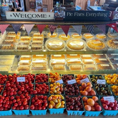 A display of colorful fruits in baskets and various pies in a bakery, with a "Welcome" sign above.