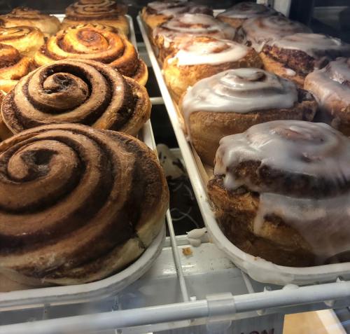 Freshly baked cinnamon rolls with swirls of cinnamon and creamy icing, displayed in a glass case.