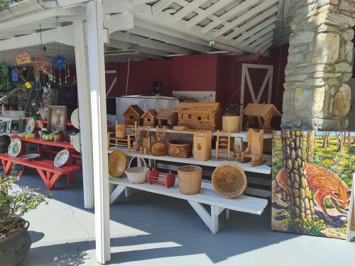 A display of wooden crafts and baskets on white shelves, with colorful artwork in the background.