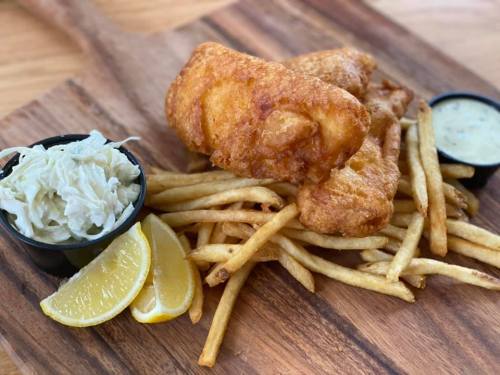Crispy fried fish fillets served with fries, coleslaw, lemon wedges, and dipping sauce on a wooden platter.