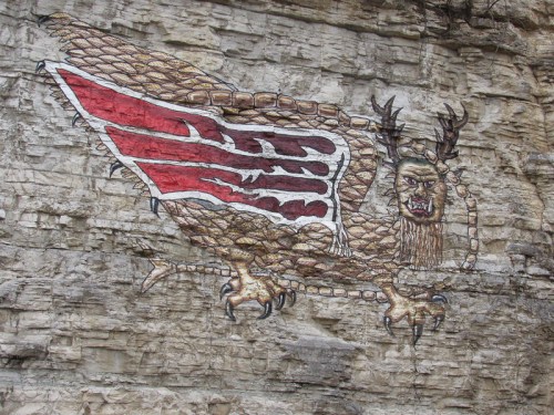 A large, colorful mural of a mythical creature with wings and antlers painted on a rocky cliff face.
