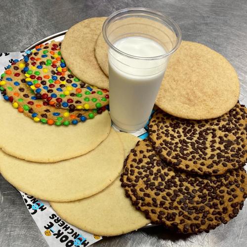 A plate of assorted cookies, including chocolate chip, sugar, and a colorful cookie, with a cup of milk.