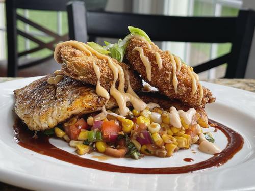 A plate featuring fried fish fillets atop a colorful corn salsa, drizzled with sauce and garnished with green onions.