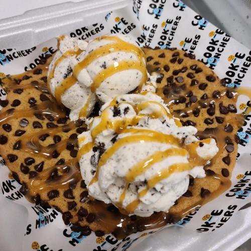 A warm chocolate chip cookie topped with two scoops of cookies and cream ice cream, drizzled with caramel sauce.