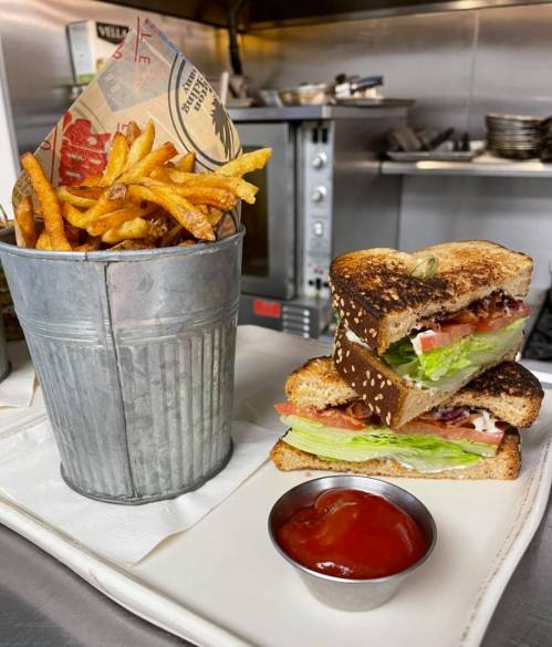 A metal bucket filled with fries next to a toasted sandwich with lettuce, tomato, and bacon, served with a side of ketchup.