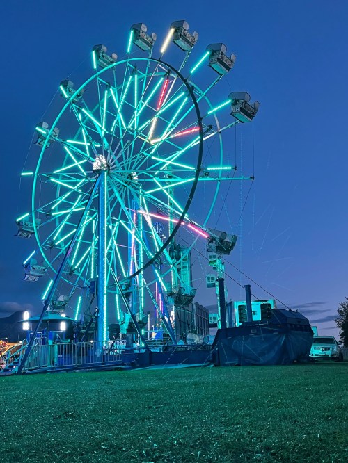 A brightly lit Ferris wheel at dusk, with colorful neon lights illuminating the sky.