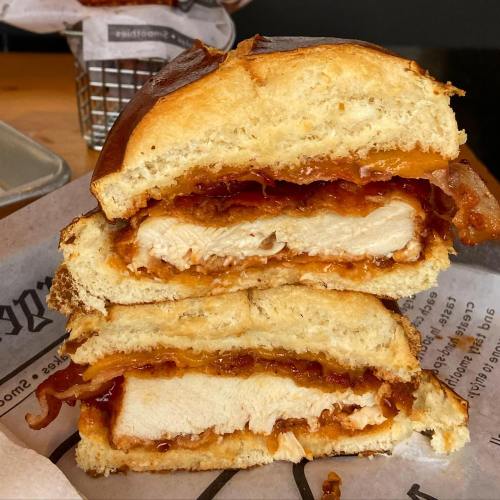 A cross-section of a crispy chicken sandwich with bacon and sauce, served on a toasted bun.