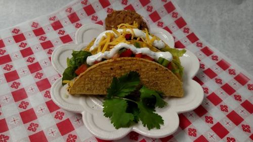 A taco filled with lettuce, tomatoes, cheese, and sour cream, served on a decorative plate with a cookie and cilantro.