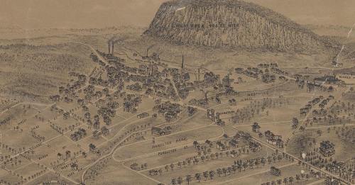 Aerial view of a historical town with buildings, factories, and a prominent mountain in the background.