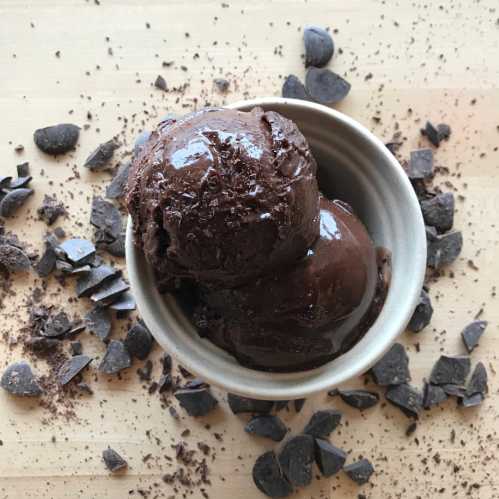 A bowl of rich chocolate ice cream surrounded by scattered chocolate shavings on a wooden surface.