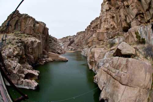 A scenic view of a rocky canyon with a calm green river flowing through it under a cloudy sky.