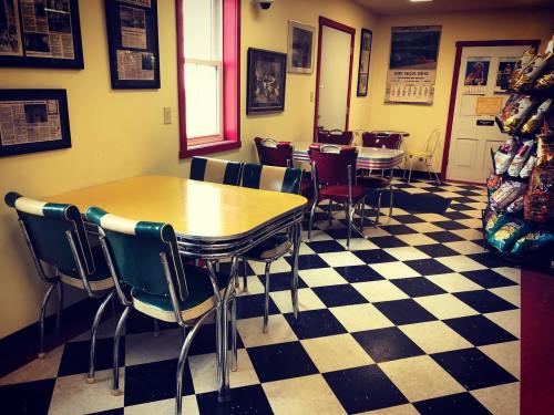A cozy diner interior with checkered floor, tables, chairs, and a snack display in the corner.