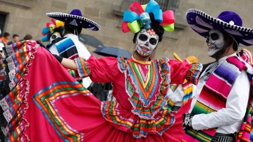 Two dancers in colorful traditional costumes celebrate with vibrant attire and painted faces during a festive event.