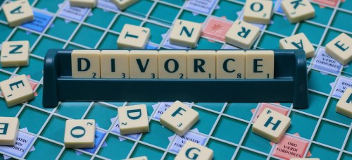 Scrabble board with tiles spelling "DIVORCE" prominently displayed among other scattered letter tiles.