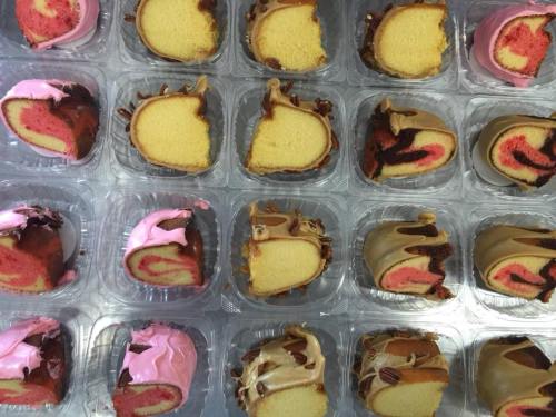A tray of assorted mini cakes, featuring pink and yellow layers with chocolate and frosting decorations.