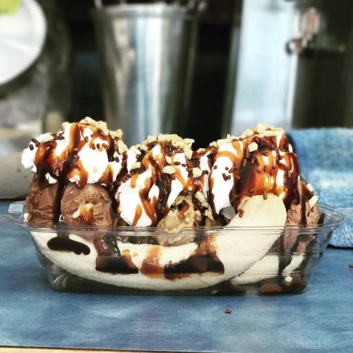 A banana split topped with chocolate and vanilla ice cream, whipped cream, nuts, and chocolate sauce in a clear dish.