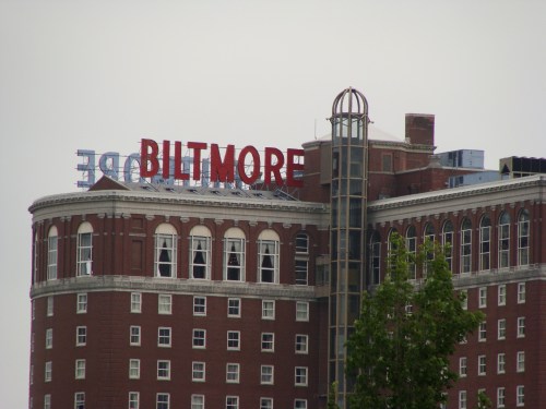 The Biltmore Hotel sign atop a historic brick building, with a cloudy sky in the background.