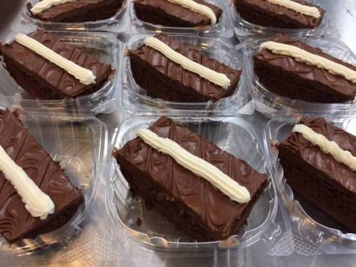 Several chocolate cake slices with frosting, arranged in clear plastic containers on a silver surface.