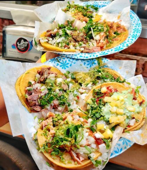 Two plates of colorful tacos topped with onions, cilantro, and various salsas, served on paper.