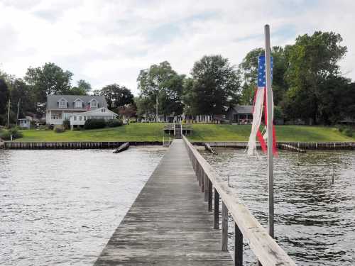 A wooden pier extends into a calm lake, with a flag and green lawns visible in the background.