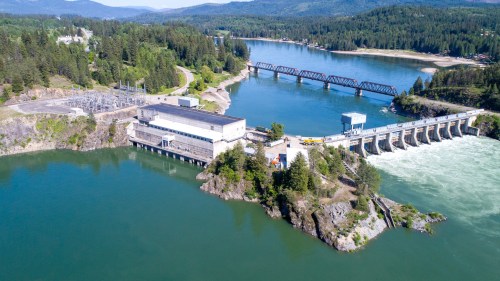 Aerial view of a dam surrounded by water, with a bridge and lush greenery in the background.
