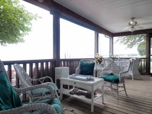 A cozy porch with wicker furniture, a table, and a view of the outdoors, surrounded by greenery.