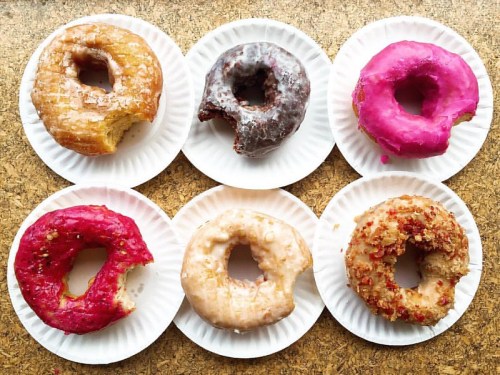 A variety of six donuts on paper plates, featuring different glazes and toppings in vibrant colors.