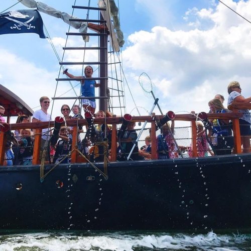 A pirate ship with people on deck, some waving and others holding nets, sailing on a sunny day.