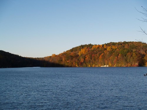 A serene lake surrounded by colorful autumn foliage and rolling hills under a clear blue sky.