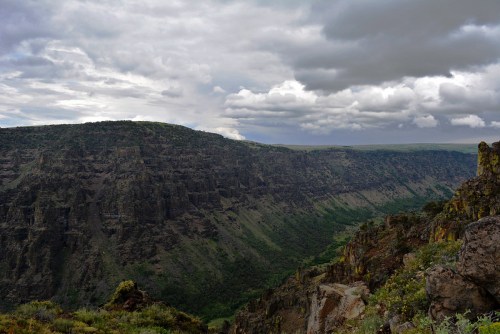 A dramatic landscape featuring steep cliffs and a lush valley under a cloudy sky.