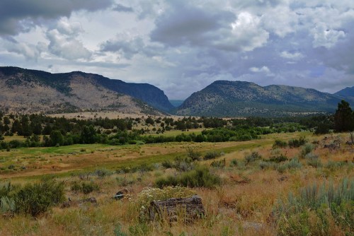 A scenic landscape featuring rolling hills, mountains, and a grassy valley under a cloudy sky.