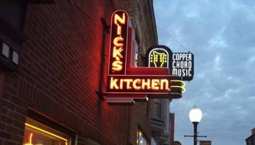 Neon sign for Nick's Kitchen and Copper Chord Music against a cloudy evening sky.