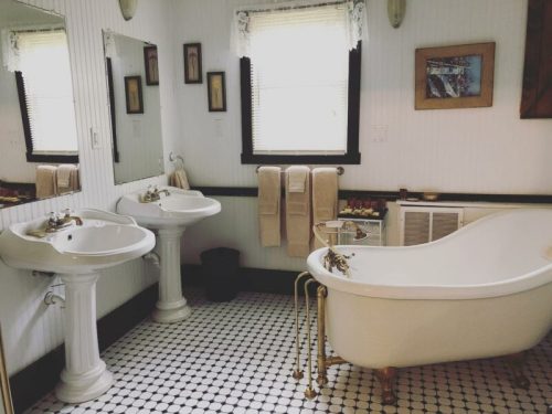 A vintage bathroom featuring a clawfoot tub, two pedestal sinks, and black-and-white tiled flooring.