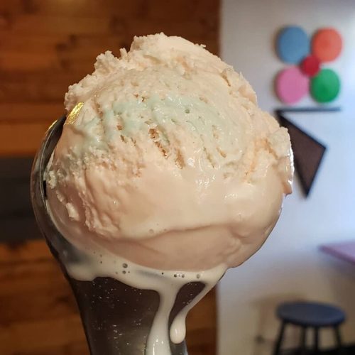 A close-up of a colorful ice cream scoop in a cone, with a creamy texture and a blurred wooden background.