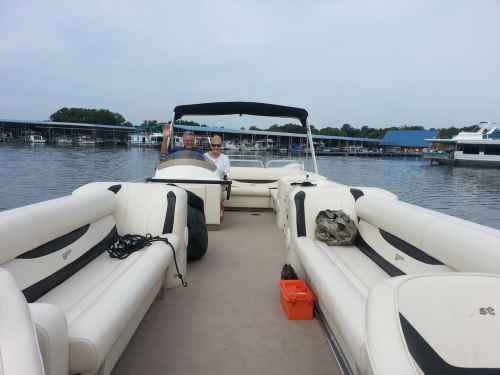 A view from the front of a boat with two people seated, surrounded by water and boat docks in the background.