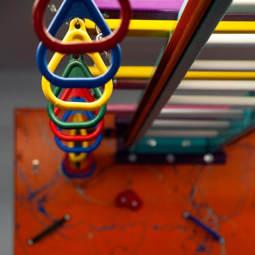 Colorful climbing rings and bars on a playground structure against an orange background.
