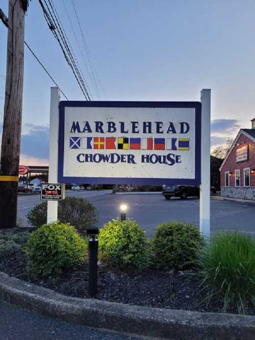 Sign for Marblehead Chowder House featuring colorful flags and a welcoming atmosphere at dusk.