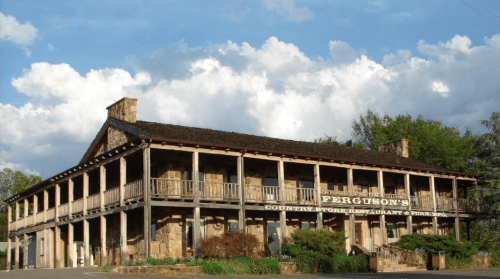 Historic stone building with a wooden balcony, featuring a sign that reads "Ferguson's Country Store, Restaurant & Hotel."