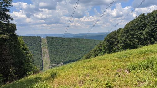 A scenic view of rolling green hills under a partly cloudy sky, with power lines stretching across the landscape.