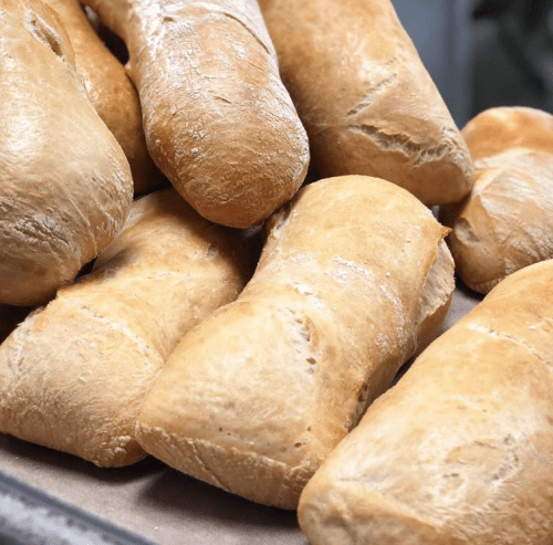 Freshly baked bread rolls stacked on a baking tray, showcasing a golden-brown crust and soft texture.