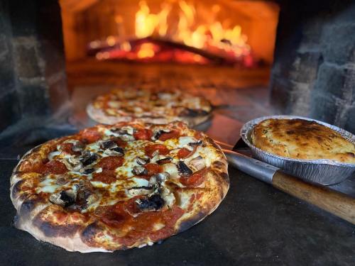 A freshly baked pizza with pepperoni and mushrooms in a wood-fired oven, alongside a pie in a metal dish.