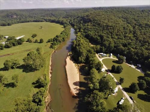 Aerial view of a winding river surrounded by lush greenery and open fields, with a campsite visible nearby.