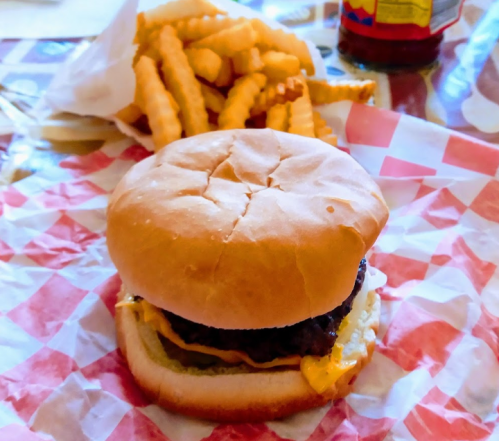 A cheeseburger with lettuce and mayonnaise on a bun, served with crinkle-cut fries in a red and white checkered wrapper.