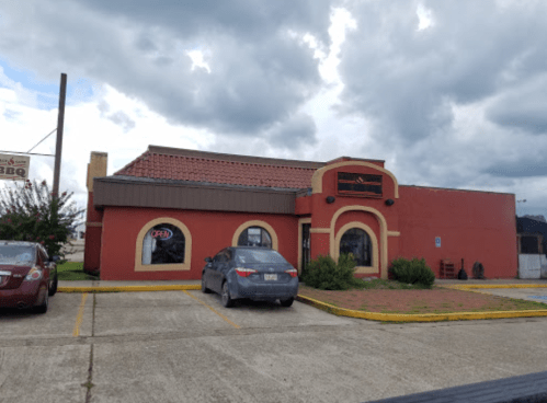 A red restaurant building with a brown roof, featuring a parking lot and cloudy sky in the background.