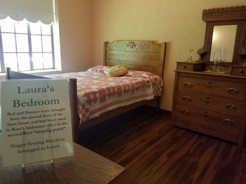 A cozy bedroom with a wooden bed, dresser, and a sign about Laura's bedroom and a Singer sewing machine.