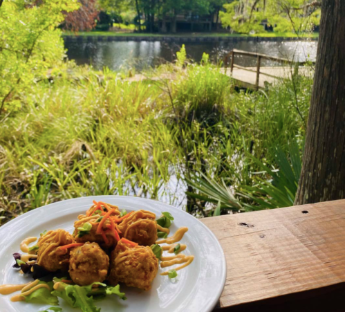 A plate of golden-brown fritters garnished with salad, set against a serene lakeside backdrop.